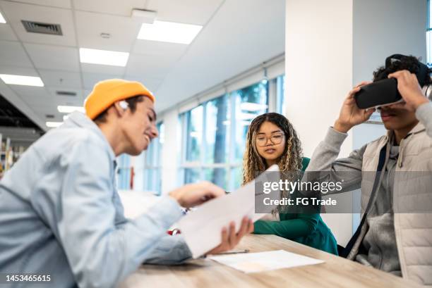 young man testing a virtual reality simulator while his friends reading the instructions at university - virtual library stock pictures, royalty-free photos & images