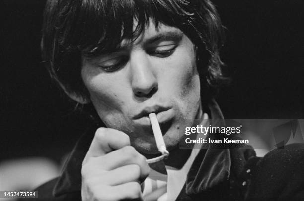 English guitarist Keith Richards of The Rolling Stones lights a cigarette during a performance by the band on the set of the Associated Rediffusion...
