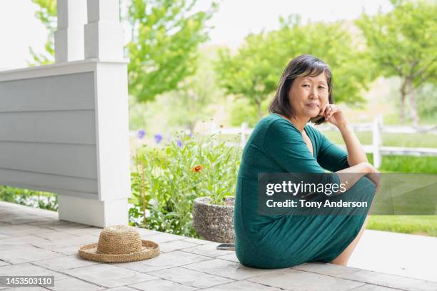 mature woman sitting on front porch looking at camera - teal portrait stockfoto's en -beelden