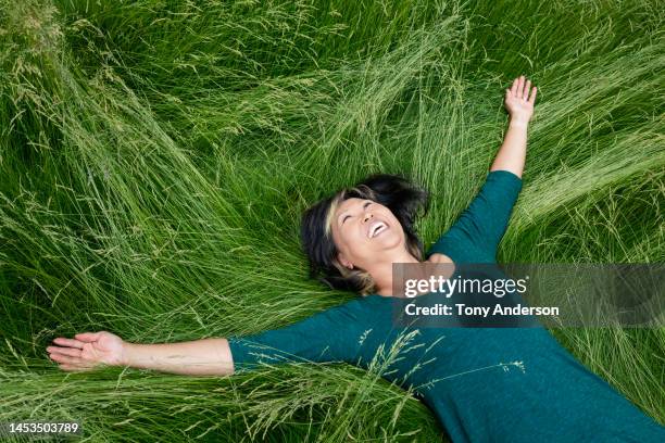 mature woman lying in tall grass laughing - grass family stock pictures, royalty-free photos & images
