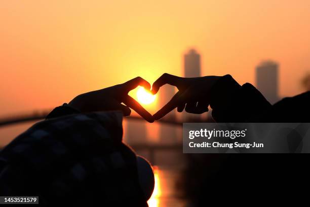 People make a heart shaped gesture as they look at the first sunrise of the year during New Year's celebrations at a park on January 1, 2023 in...