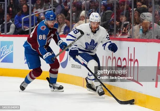 Michael Bunting of the Toronto Maple Leafs handles the puck along the boards against Andreas Englund of the Colorado Avalanche during the first...