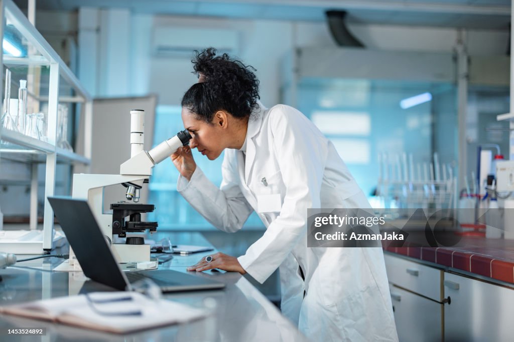 Femme scientifique regardant au microscope et utilisant un ordinateur portable dans un laboratoire