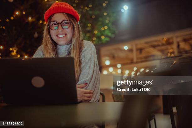 cheerful woman looking directly into camera while sitting in hotel lobby in front of laptop - christmas finland stock pictures, royalty-free photos & images