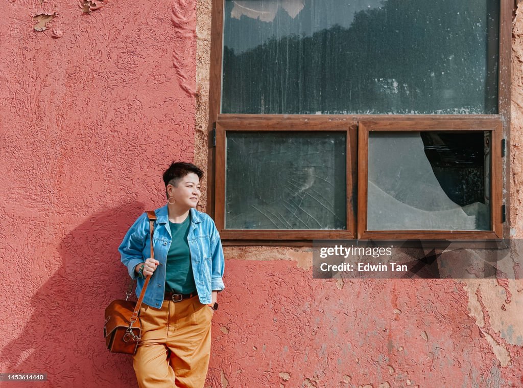 Asian Chinese female tourist leaning on wall looking away smiling in Forêt Toufliht, Morocco rural scenery
