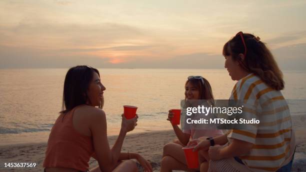 group of young asian women celebrating and drinking alcohol on tropical beach at sunset. - evening indulgence stock pictures, royalty-free photos & images