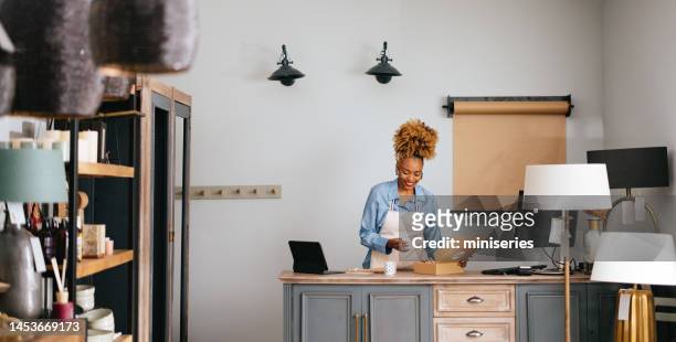 happy woman packing order in a cardboard box in a home decor store - small business owners stock pictures, royalty-free photos & images