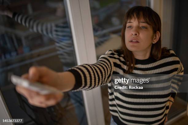 young woman turning on air conditioner - bijstellen stockfoto's en -beelden