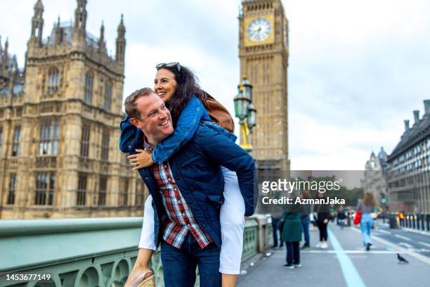 a caucasian adult male carrying his caucasian girlfriend on his back while they are exploring london - couple london stockfoto's en -beelden