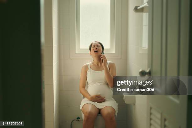 asian mother pregnant using phone urgent calling husband her feeling pain and first sign to giving birth at home - labour childbirth stock pictures, royalty-free photos & images