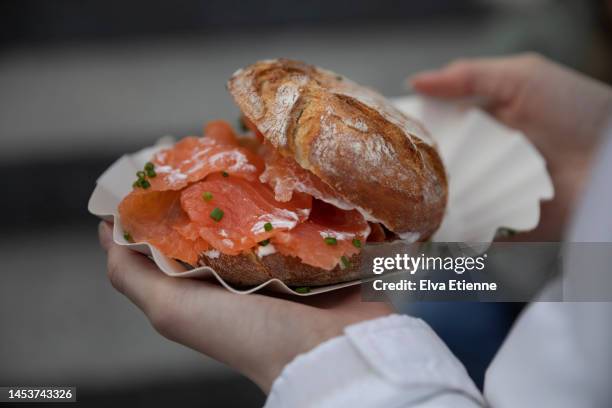 close-up of freshly smoked salmon on a bread roll in a paper tray held by a teenager at a german christmas market. - duitse gerechten stockfoto's en -beelden