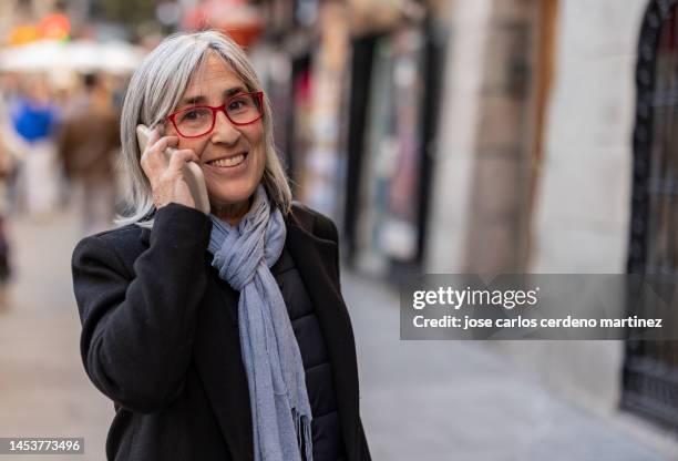 she strolls through the city, the woman with salt and pepper hair checks her mobile phone for updates - holding phone to ear stock pictures, royalty-free photos & images