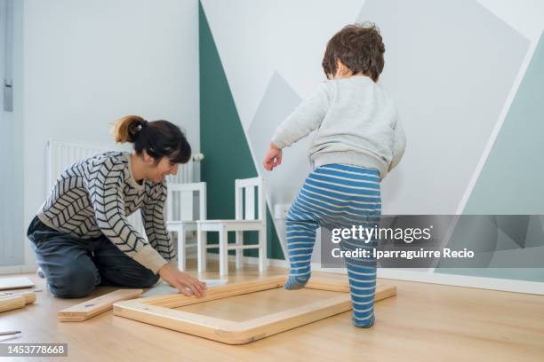 mother and son having fun assembling a piece of furniture in the new renovated baby's room, assembling a drawing table for the child - furniture maker stockfoto's en -beelden