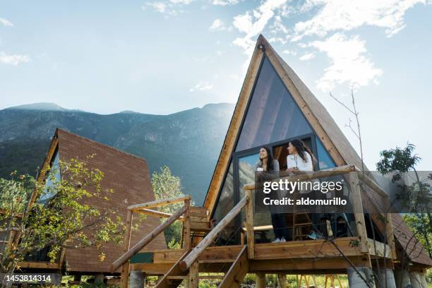 two female friends enjoying hot drink outside of cabin - holiday villa bildbanksfoton och bilder