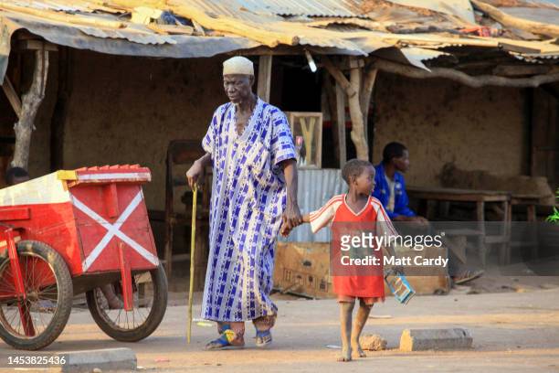 An elderly man holds the hand of a young boy as they look to cross the road on, January 24, 2010 in Ouagadougou, Burkina Faso. Landlocked Burkina...