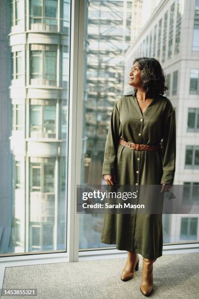 portrait of businesswoman looking out of  window across the city - women in long dress stock pictures, royalty-free photos & images