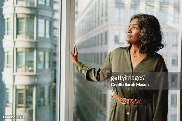 portrait of businesswoman standing with hand against office window looking out - enterprise stock pictures, royalty-free photos & images