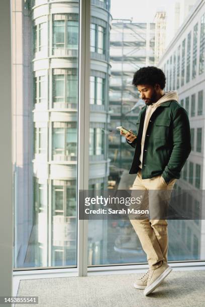 Portrait of young man standing against office window looking at mobile phone