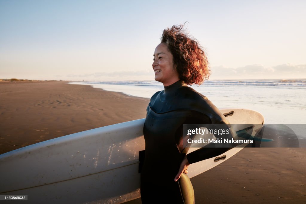 Side view portrait of a woman standing in the surf with a surfboard under her arm.
