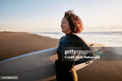 Side view portrait of a woman standing in the surf with a surfboard under her arm. Side view portrait of a woman standing in the surf with a surfboard under her arm.
