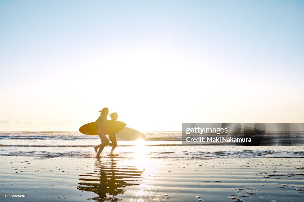 Side view of a couple running in the surf with surfboards.