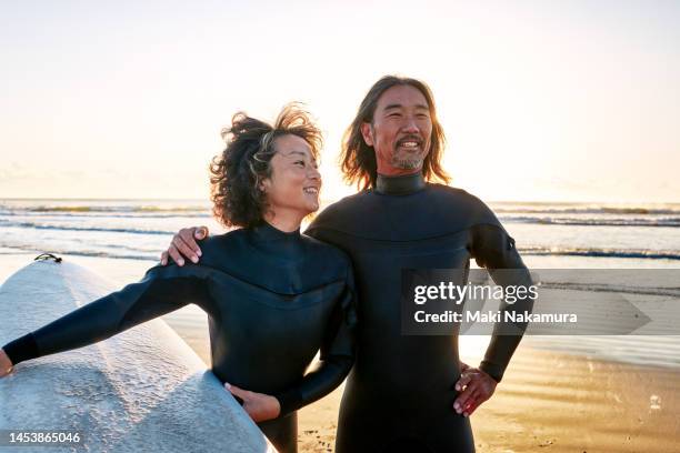 portrait of a woman holding a surfboard and a man with his hand around her shoulder. - what is shoulder surfing stock pictures, royalty-free photos & images