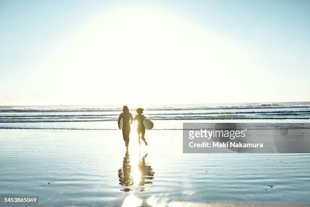 a couple running to the ocean with surfboards. - mental wellbeing foto e immagini stock