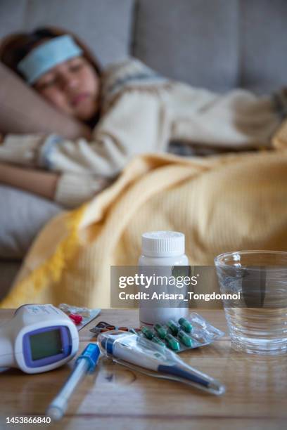 sick influenza girl woman lying on the sofa and there is a fever meter and medicine on the table - coronavirus fever stock pictures, royalty-free photos & images