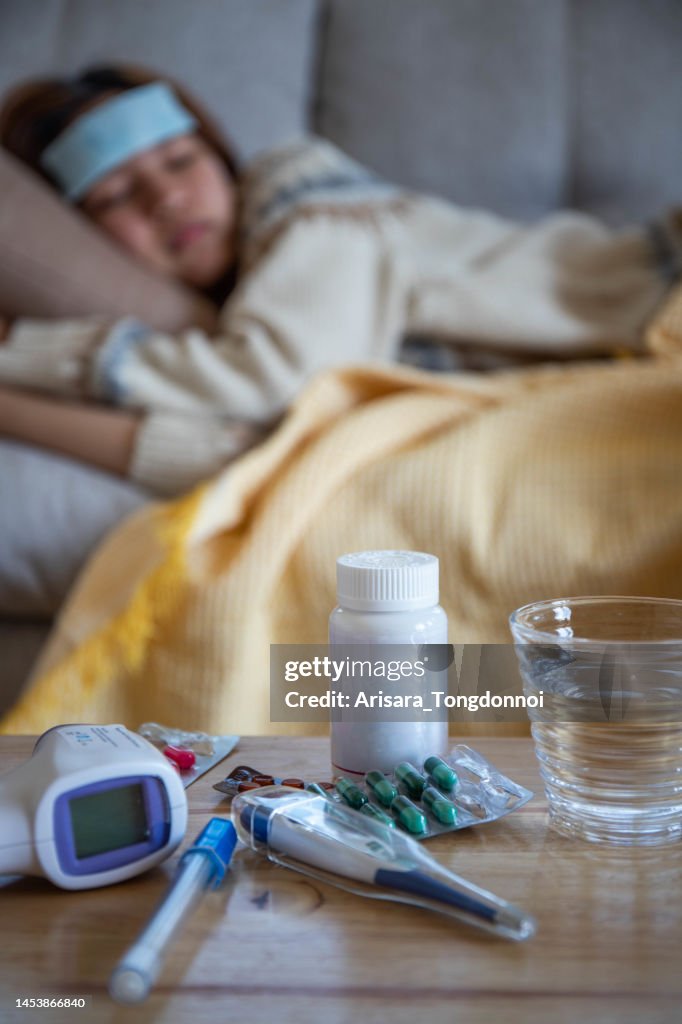 Mulher doente da menina da gripe deitada no sofá E há um medidor de febre e remédio na mesa