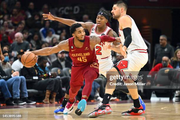 Donovan Mitchell of the Cleveland Cavaliers passes around Nikola Vucevic and Ayo Dosunmu of the Chicago Bulls during the second half at Rocket...