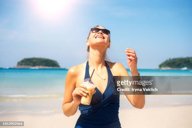 beautiful young woman feels happy and enjoying of drinking the ice coffee during summer holidays on a sea tropical beach. - women tanning beach drink stock-fotos und bilder
