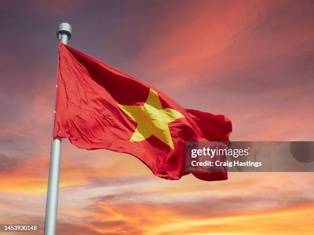 hanoi, vietnam - vietnamese flag flowing in the wind on a sunset background - vietnam flag stock pictures, royalty-free photos & images