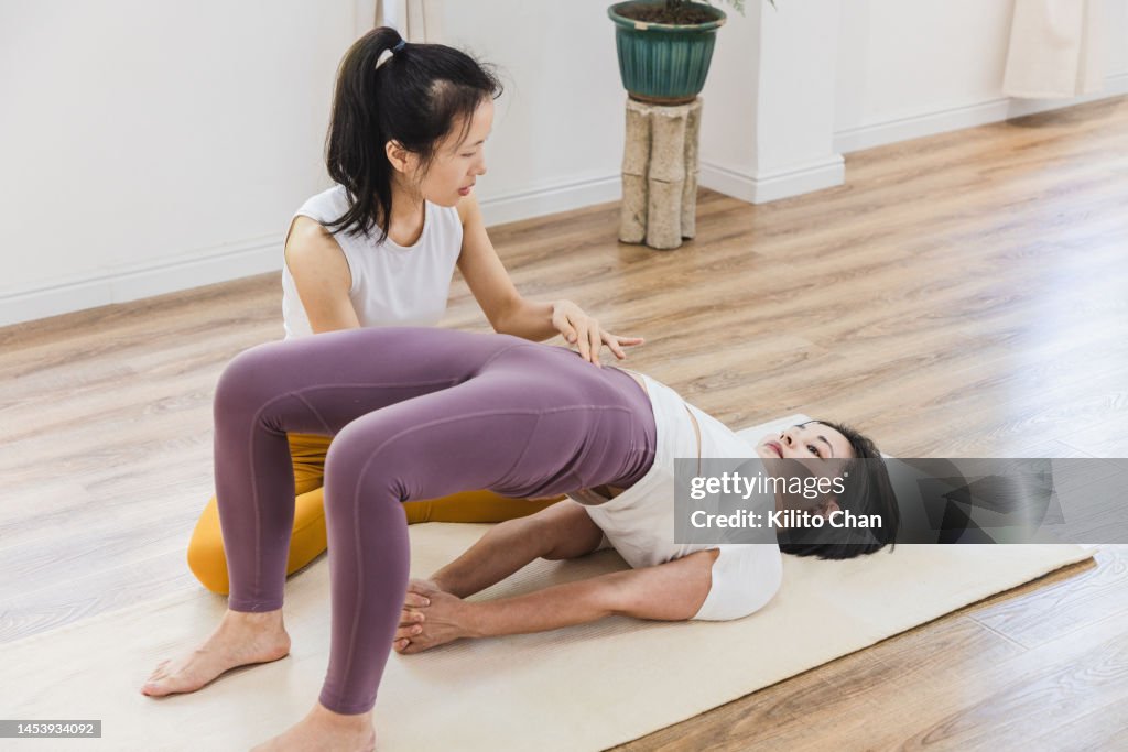 Asian yoga instructor coaching student in a yoga studio