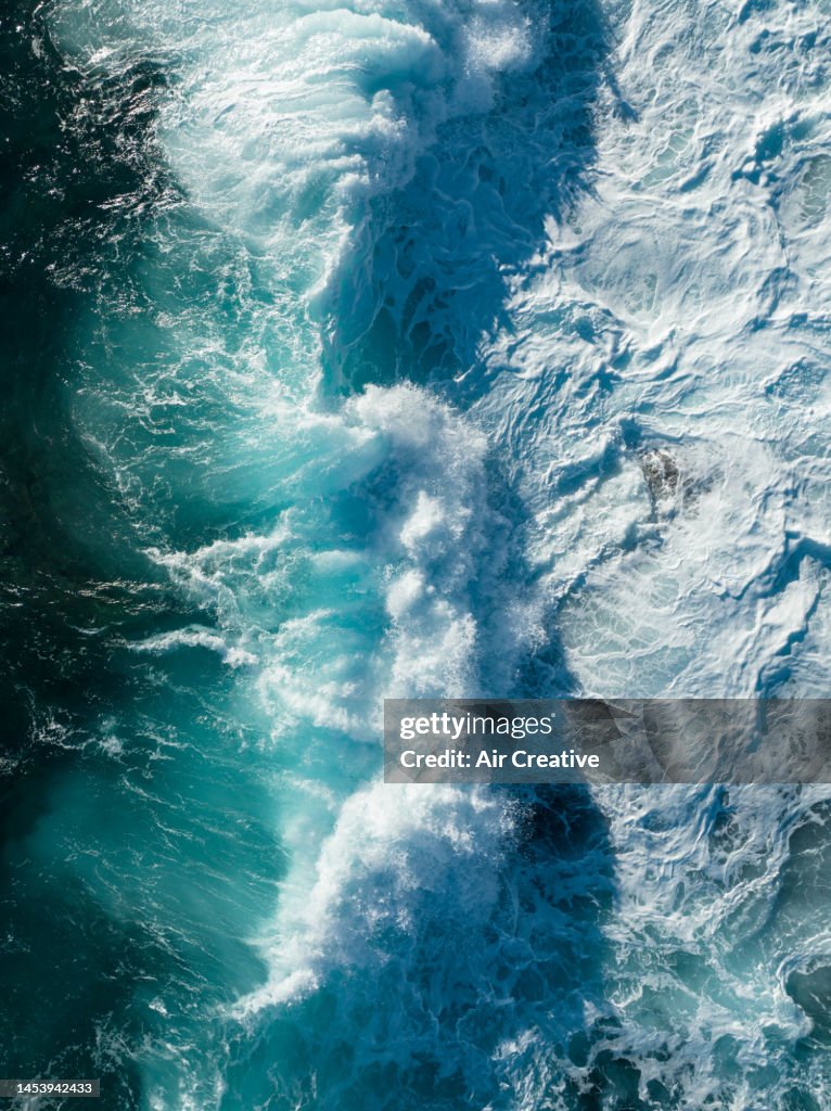 Top-down aerial view of waves breaking on the coastline during a strong wind day