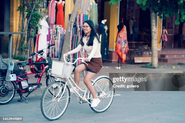 smiling young woman riding bicycle on bridge in hoi an, vietnam - bicycle rental stockfoto's en -beelden