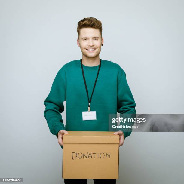 young volunteer holding donation box - man holding donation box stock pictures, royalty-free photos & images