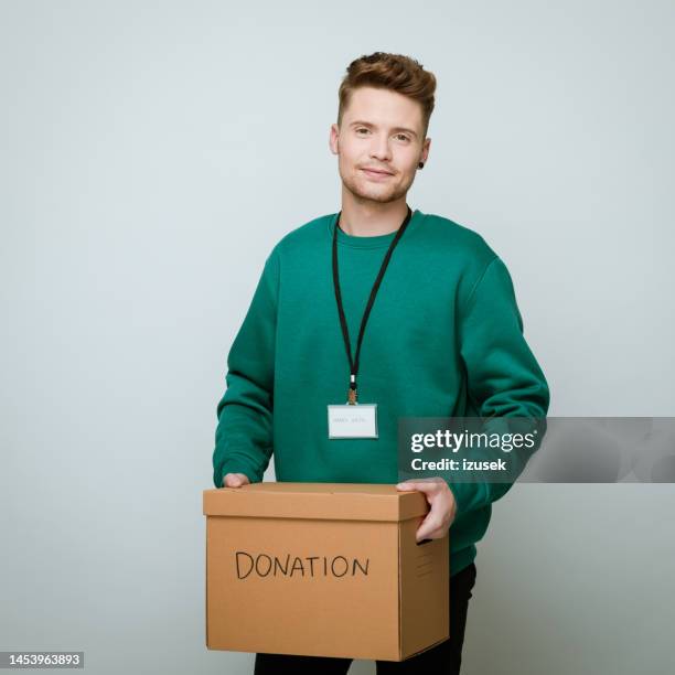 young volunteer holding donation box - man holding donation box stock pictures, royalty-free photos & images