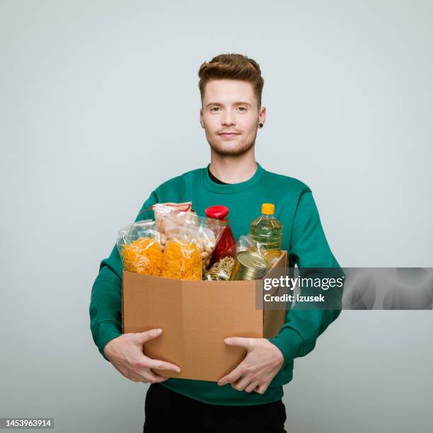 young volunteer holding donation box of food - man holding donation box stock pictures, royalty-free photos & images