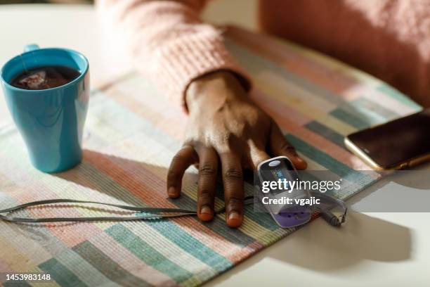 a black woman measures her oxygen level at home using a pulse oximeter - pulse trace stock pictures, royalty-free photos & images