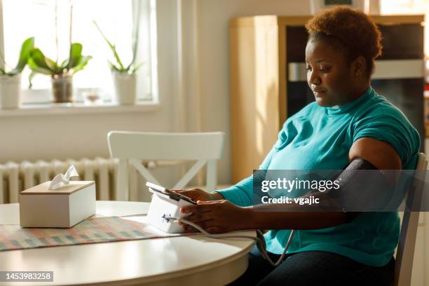 young woman checks her blood pressure at home - bloeddrukmeter stockfoto's en -beelden