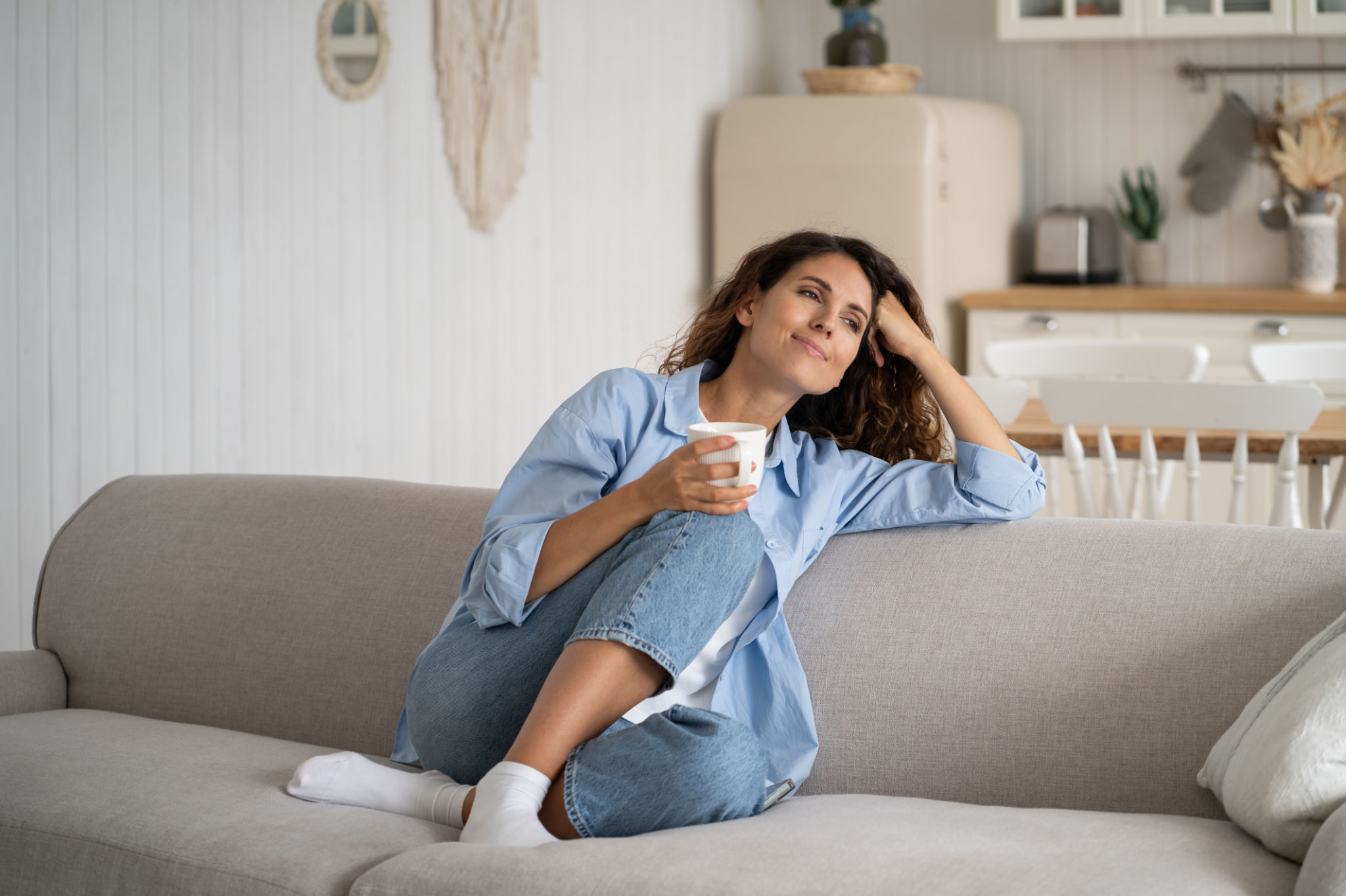 Young happy relaxed woman sitting on sofa enjoying quiet moments at home with cup of tea or coffee Young happy relaxed woman sitting on sofa enjoying quiet moments at home with cup of tea or coffee