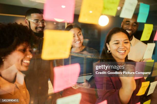 geschäftsleute lachen beim brainstorming mit klebenotizen an einem bürofenster - brainstorming stock-fotos und bilder