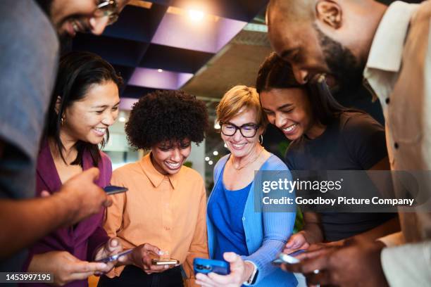 smiling businesspeople sharing files wirelessly with their phones in an office - partilha de ficheiros imagens e fotografias de stock