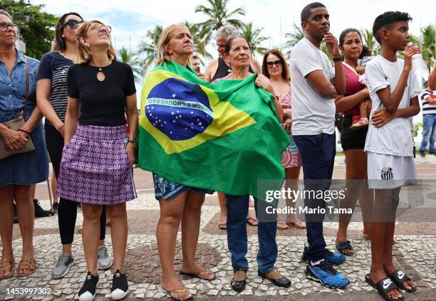 People await the arrival of the coffin of football legend Pelé as it is transported in a funeral procession through the streets of Santos on the way...