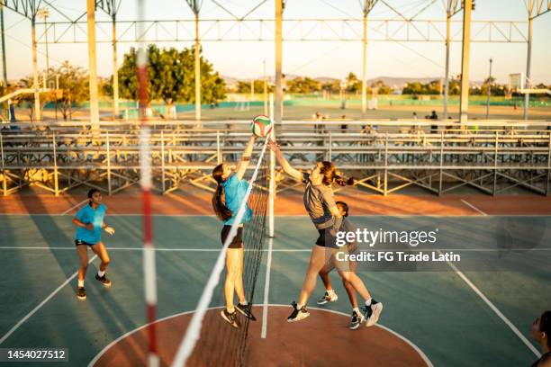 female volleyball player spiking the ball while other team defending at sports court - candid volleyball stock pictures, royalty-free photos & images