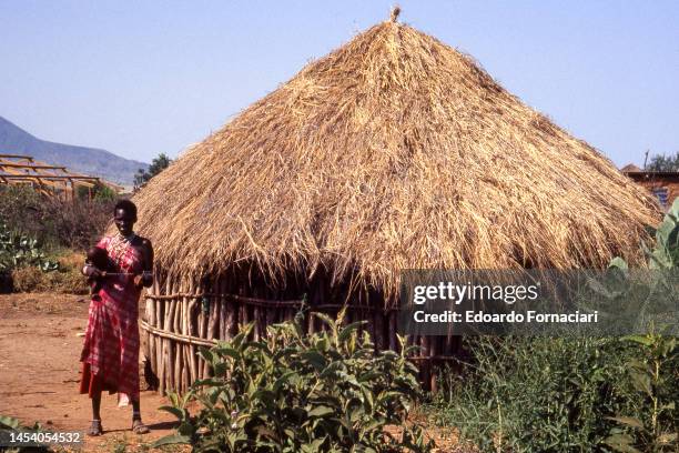 View of an unidentified woman as she stands, holding an infant, outside a hut in a Maasai village, Shompole, Kenya, April 10, 2002.