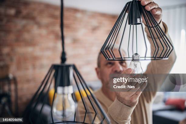 a man changes a light bulb in an apartment by himself - installing ceiling light fixture stock pictures, royalty-free photos & images