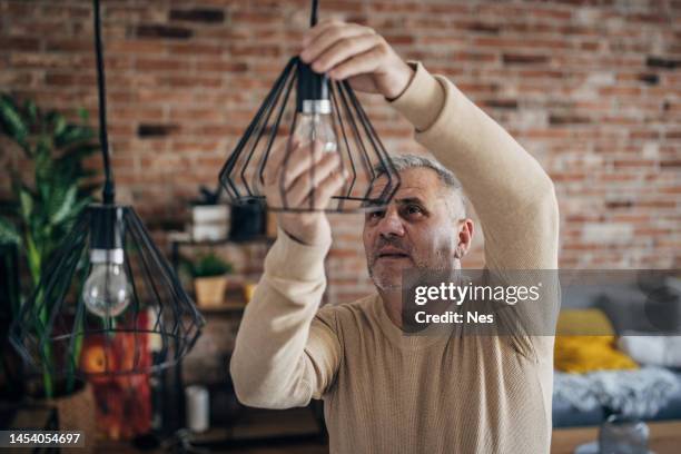a man changes a light bulb in an apartment by himself - lampje-vervangen stockfoto's en -beelden
