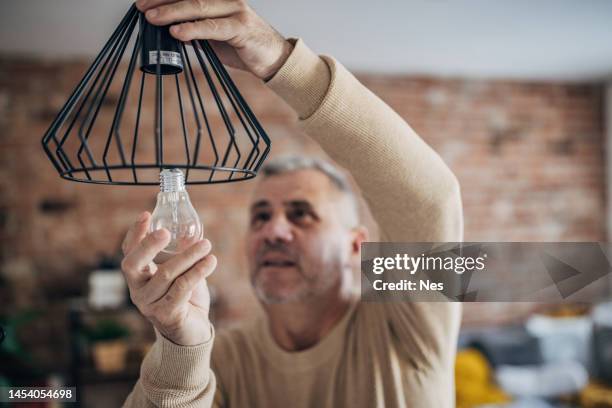 a man changes a light bulb in an apartment by himself - installing ceiling light fixture stock pictures, royalty-free photos & images