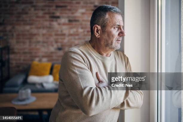 un vieil homme solitaire regarde par la fenêtre - être seul photos et images de collection